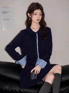 Woman in a navy blue knit two-piece set, seated and holding a small silver device.