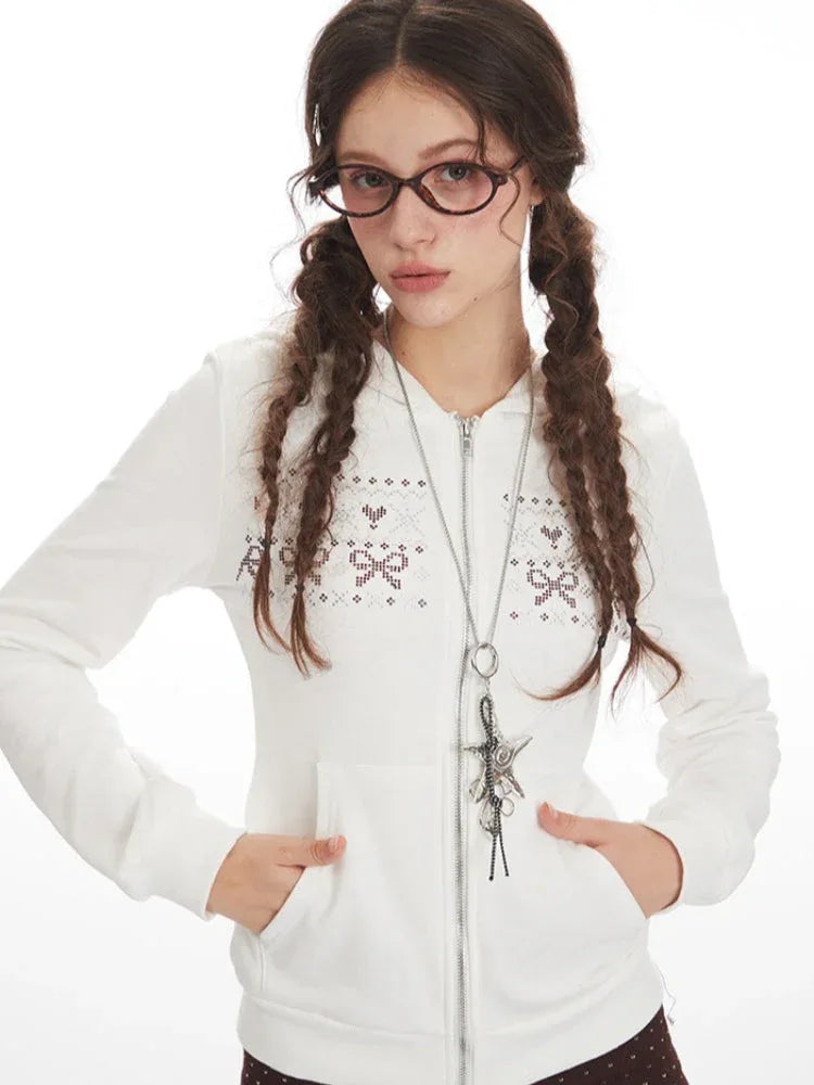 Close-up of a woman's face wearing a white zip-up hoodie with a decorative pattern, and glasses.