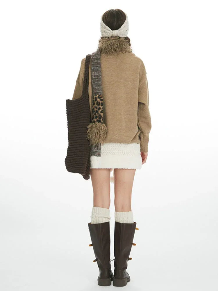 Back view of a woman wearing a brown sweater with a bird and star pattern, a white textured skirt, cream leg warmers, and brown boots. Secondary image