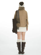 Back view of a woman wearing a brown sweater with a bird and star pattern, a white textured skirt, cream leg warmers, and brown boots.