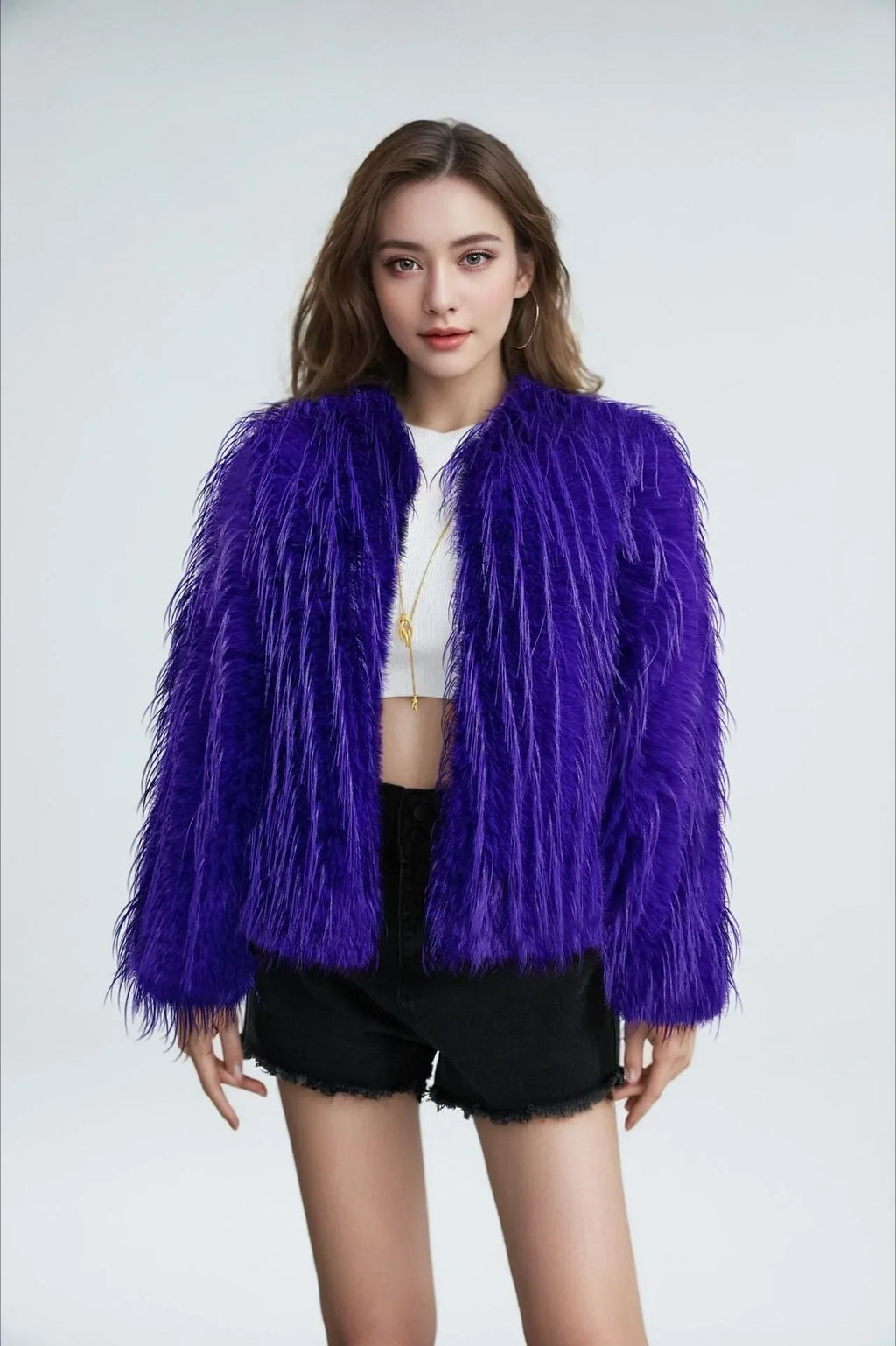 Model wearing a purple faux fur jacket with a fringed texture, a cropped length, and an open front, paired with a white crop top and black shorts.