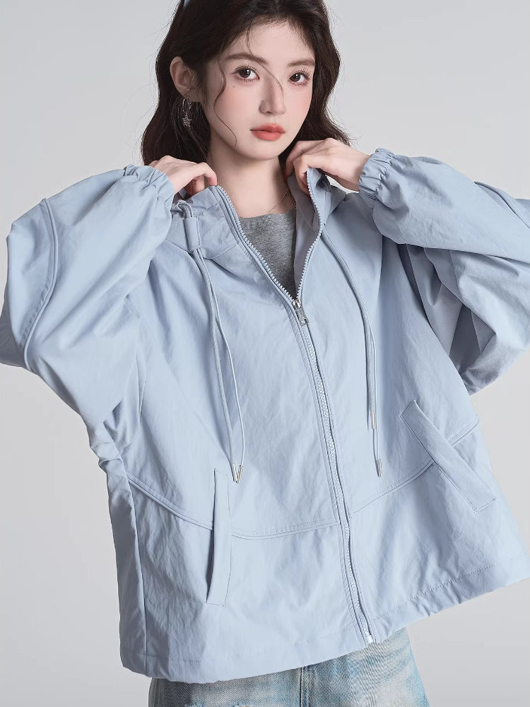 Woman adjusting the hood of a light blue jacket, showing the zipper detail.