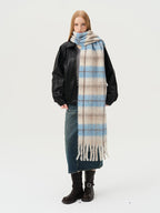 Model wearing a black jacket, grey top, denim skirt, and a long blue and beige plaid scarf with fringe