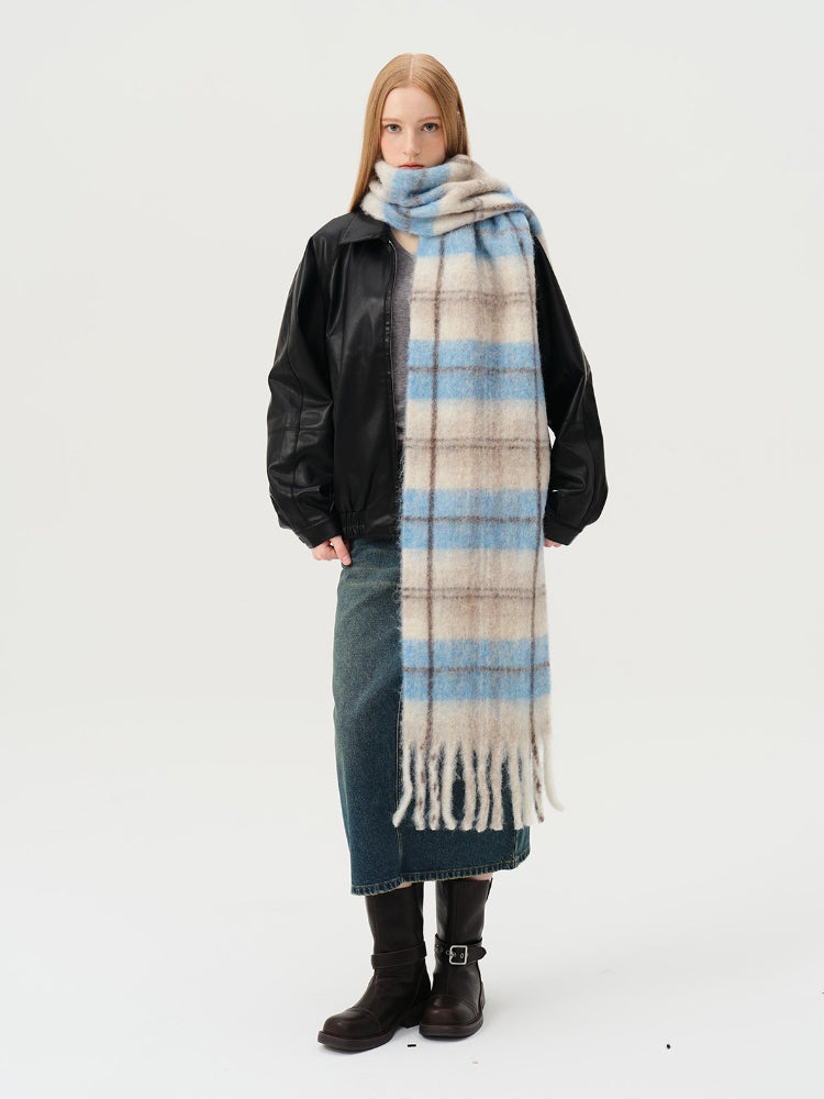 Model wearing a black jacket, grey top, denim skirt, and a long blue and beige plaid scarf with fringe