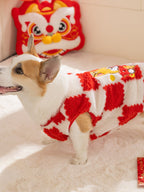 Side view of a corgi dog wearing a red and white checkered plush sweater, with a decorative pillow and lion head cushion in the background.