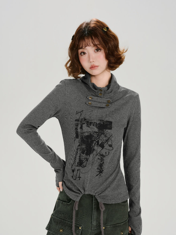 Woman wearing a grey long-sleeve graphic print turtleneck top with thumbhole cuffs and a drawstring hem, posing with one hand on her hip.