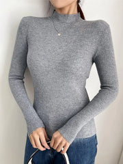 Front view of a woman in a gray ribbed mock neck long sleeve sweater and blue jeans holding a magazine