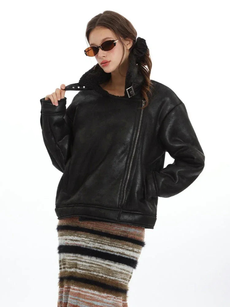 Close-up of a model wearing a black faux leather jacket with shearling lining, adjusting the collar.