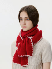Woman wearing a red knit scarf with white contrast stitching over a cream cable knit sweater, profile view looking left.