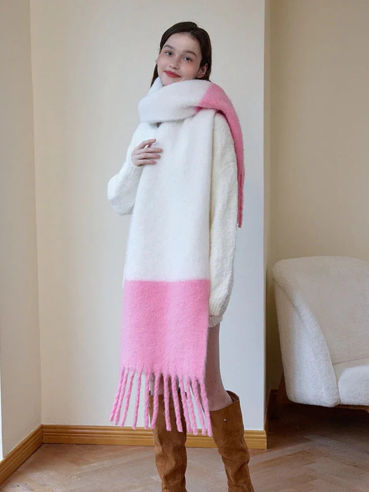 Woman wearing a white sweater and a long white and pink two-tone fuzzy knit scarf with fringe trim, draped to one side.