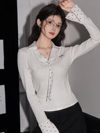 Close-up of a woman's face wearing glasses and a white ribbed long-sleeve shirt with polka dot cuffs.