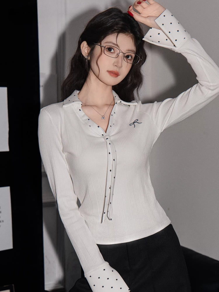 Close-up of a woman's face wearing glasses and a white ribbed long-sleeve shirt with polka dot cuffs.