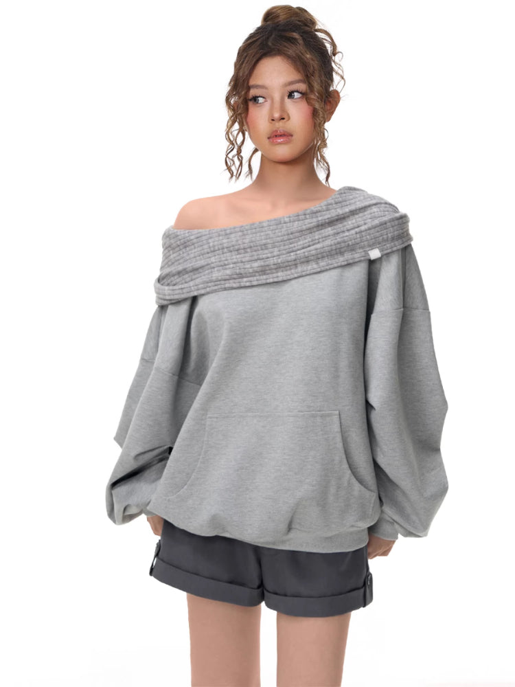 Three-quarter view of a model in a grey off-the-shoulder sweatshirt with a ribbed neckline and voluminous sleeves.