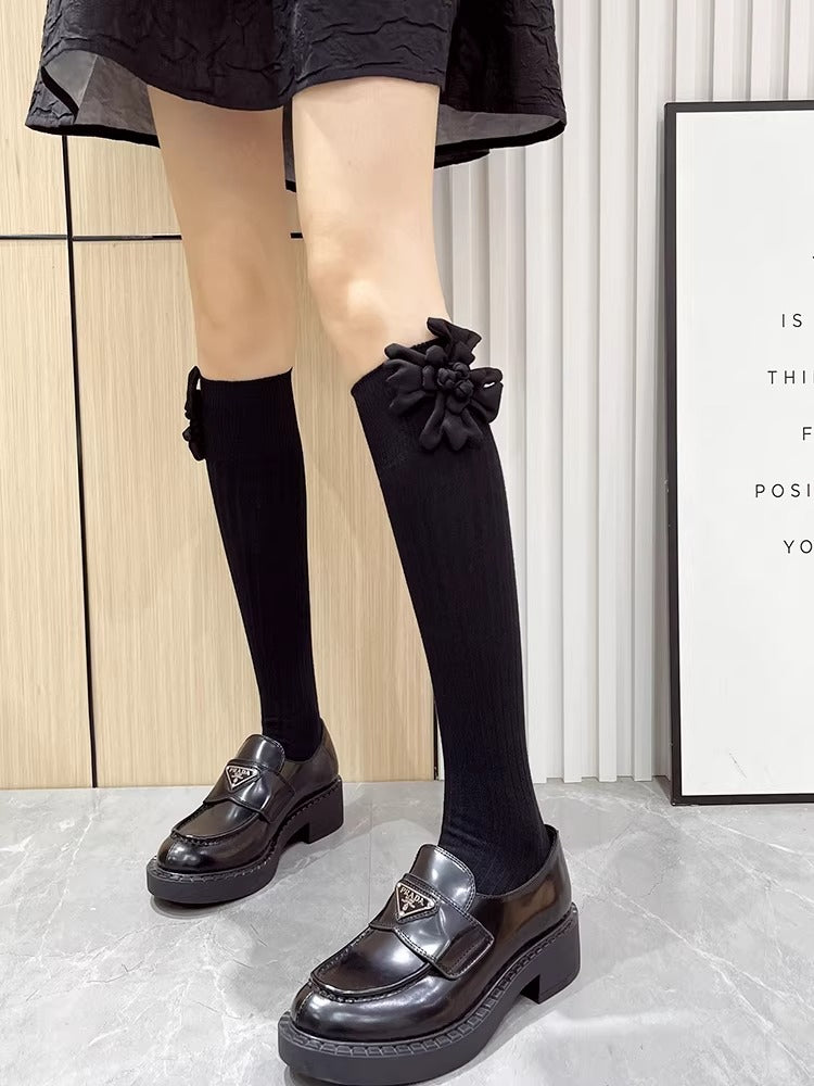 Model wearing black knee-high socks with flower embellishments and platform loafers.