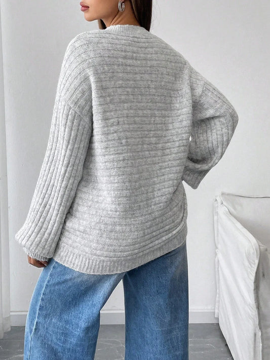 Back view of a woman wearing a light grey oversized knit sweater with balloon sleeves and a crew neck, paired with blue denim jeans.