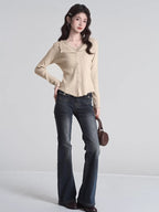 Full body shot of a woman wearing a beige ribbed knit cardigan with lace trim and dark wash flare jeans.