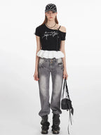 Woman wearing a black off-the-shoulder top with white ruffle trim and grey jeans, holding a black handbag.