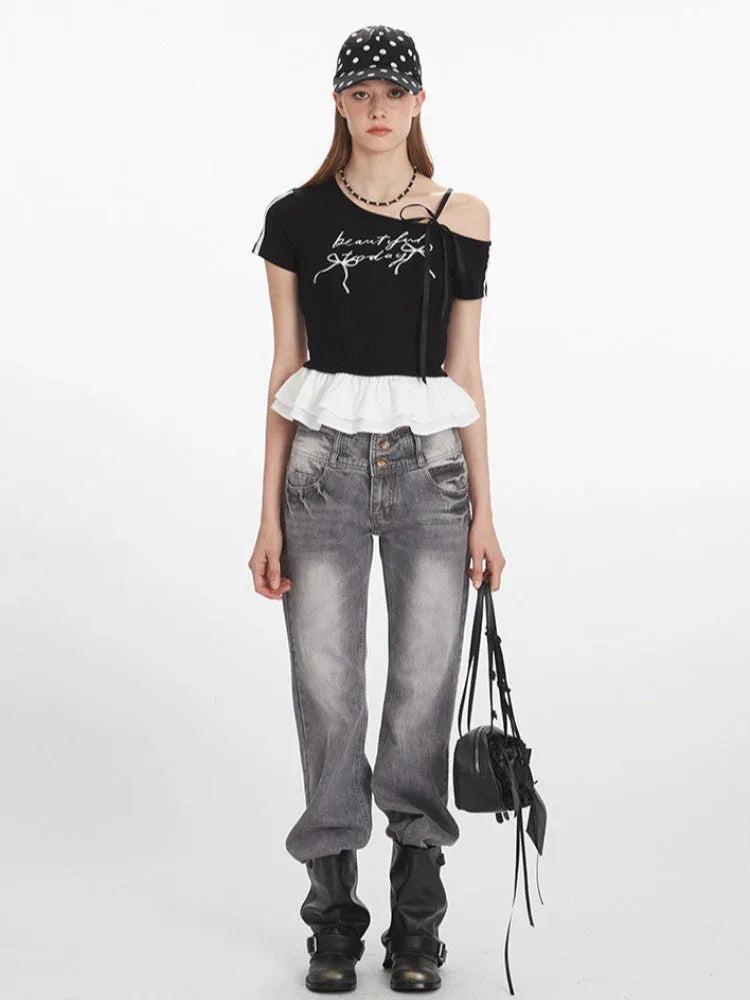 Woman wearing a black off-the-shoulder top with white ruffle trim and grey jeans, holding a black handbag.