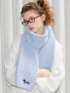 A young woman poses with a light blue fuzzy knit scarf with an embroidered dog detail.