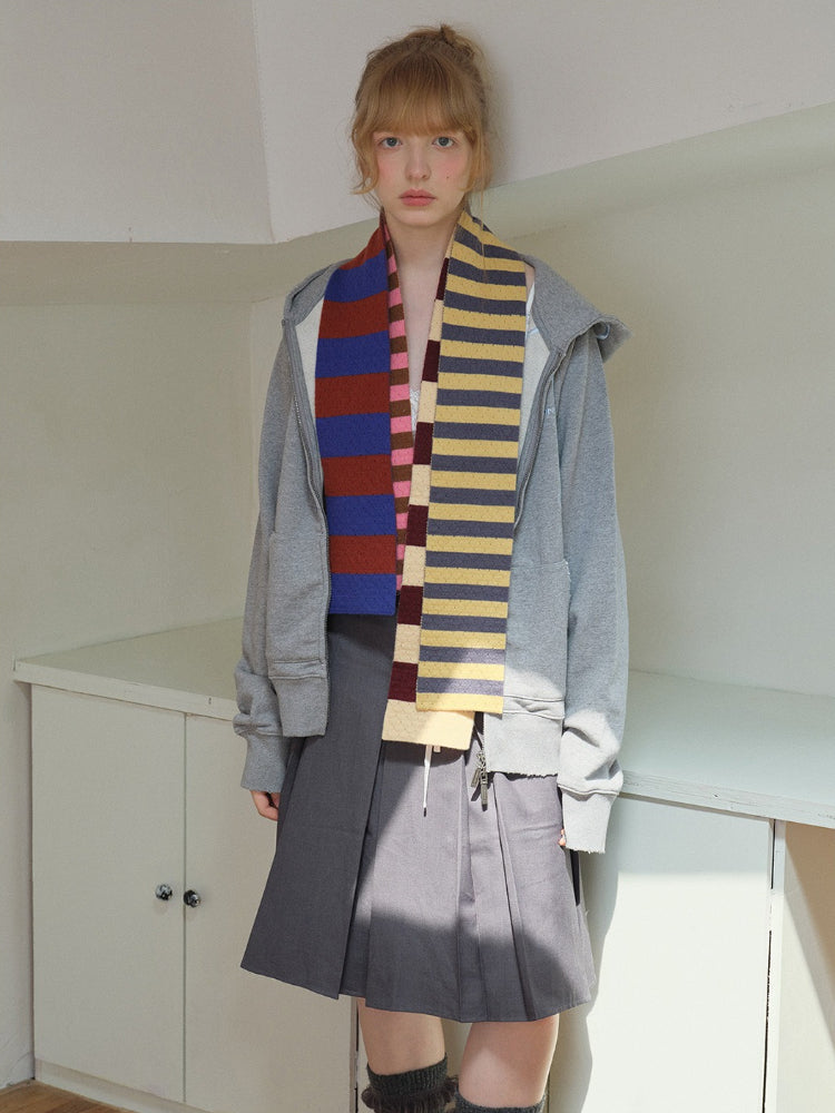 Model wearing a grey zip-up hoodie, grey pleated skirt, and a striped scarf.