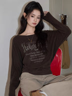 Woman posing with a brown long-sleeved graphic t-shirt.