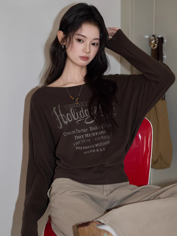 Woman posing with a brown long-sleeved graphic t-shirt.