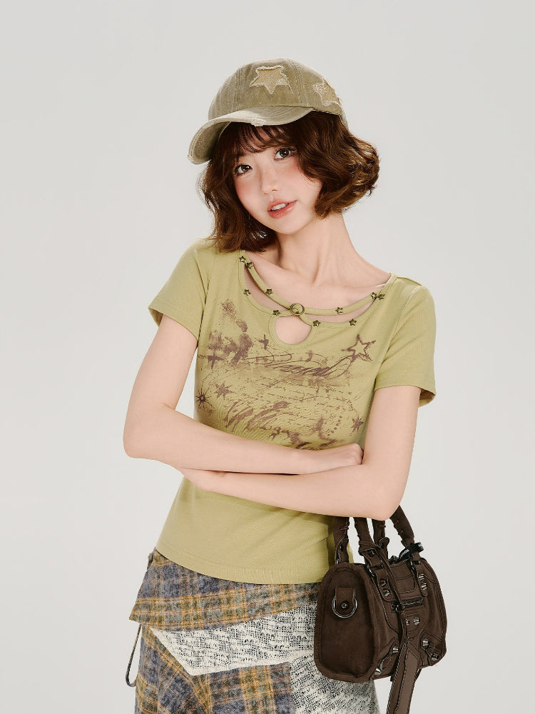 Model wearing a light green short-sleeve t-shirt with a cutout neckline and star details, paired with an asymmetrical plaid skirt and a khaki baseball cap, holding a brown handbag.