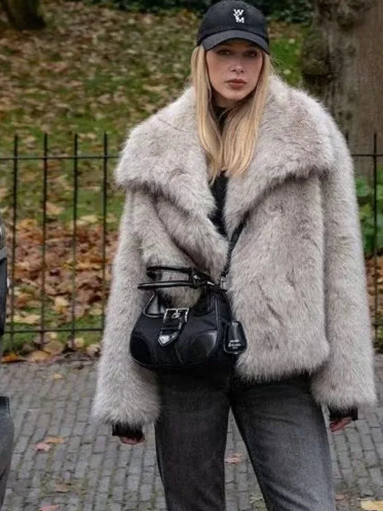 Woman wearing a light grey oversized faux fur jacket with black jeans and a black handbag