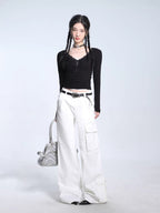 Full-body shot of a model in a black ribbed long-sleeve top, white cargo pants, and a silver handbag.
