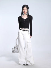 Full-body shot of a model in a black ribbed long-sleeve top, white cargo pants, and a silver handbag.