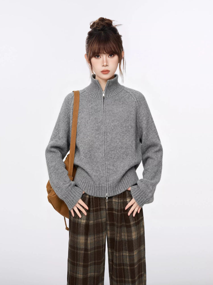 Woman wearing a grey zip-up knit sweater and brown plaid wide-leg pants, with hands on hips.