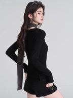 Woman wearing a black long-sleeved top with a grey asymmetrical overlay and scarf detail, shown from the back.