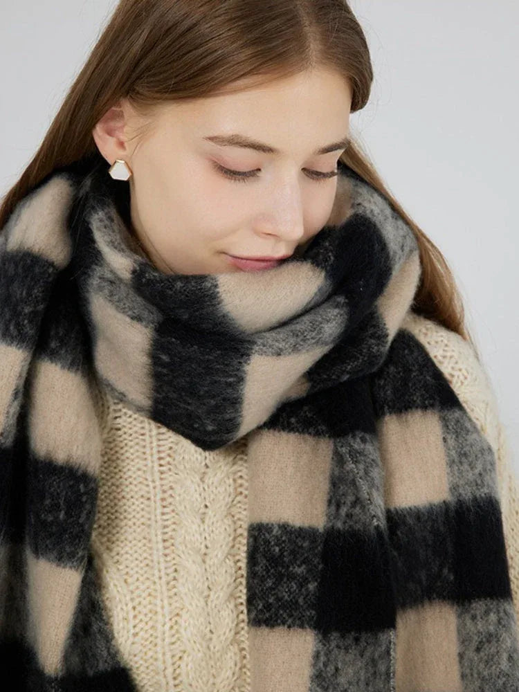 Close-up of a woman wearing a cream cable knit sweater and a large black and beige plaid scarf with fringe around her neck.