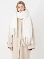 Woman wearing a white fluffy scarf draped over a beige coat, front view