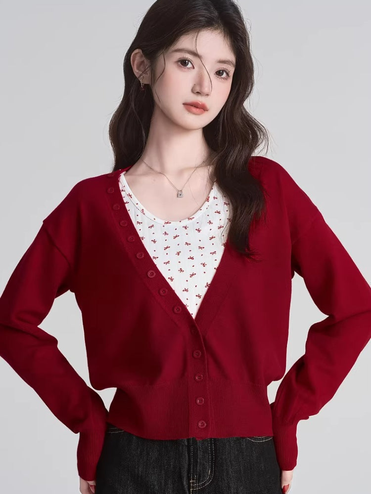 Woman wearing a red V-neck button-down cardigan over a white floral print tank top.