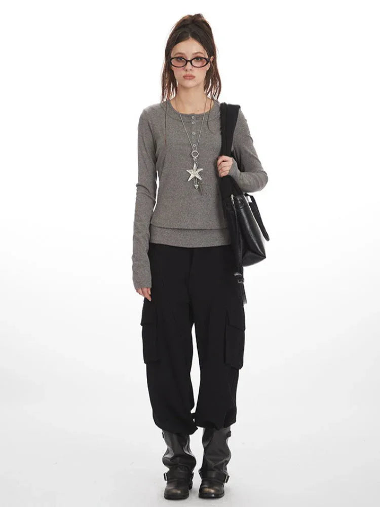Woman wearing a grey long-sleeved shirt with a layered hem, black cargo pants, black boots, and a black shoulder bag.