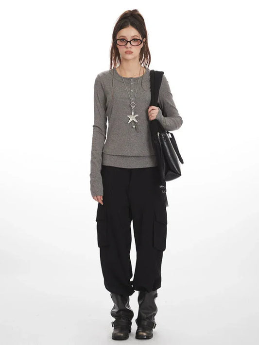 Woman wearing a grey long-sleeved shirt with a layered hem, black cargo pants, black boots, and a black shoulder bag.