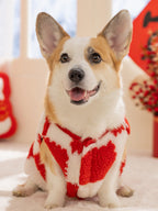 Corgi dog wearing a red and white checkered plush sweater with a festive design, sitting indoors.
