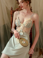 Woman in a light green satin slip dress with lace detailing, holding a decorative hand mirror.
