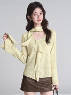 Woman wearing a light yellow textured knit top with a draped neckline and bell sleeves, paired with a brown mini skirt.
