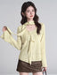 Woman wearing a light yellow textured knit top with a draped neckline and bell sleeves, paired with a brown mini skirt.