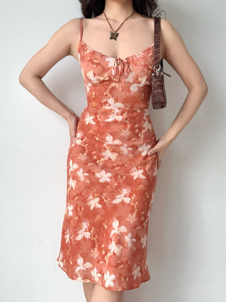 Woman wearing a floral print midi slip dress with spaghetti straps and a tie-front detail.