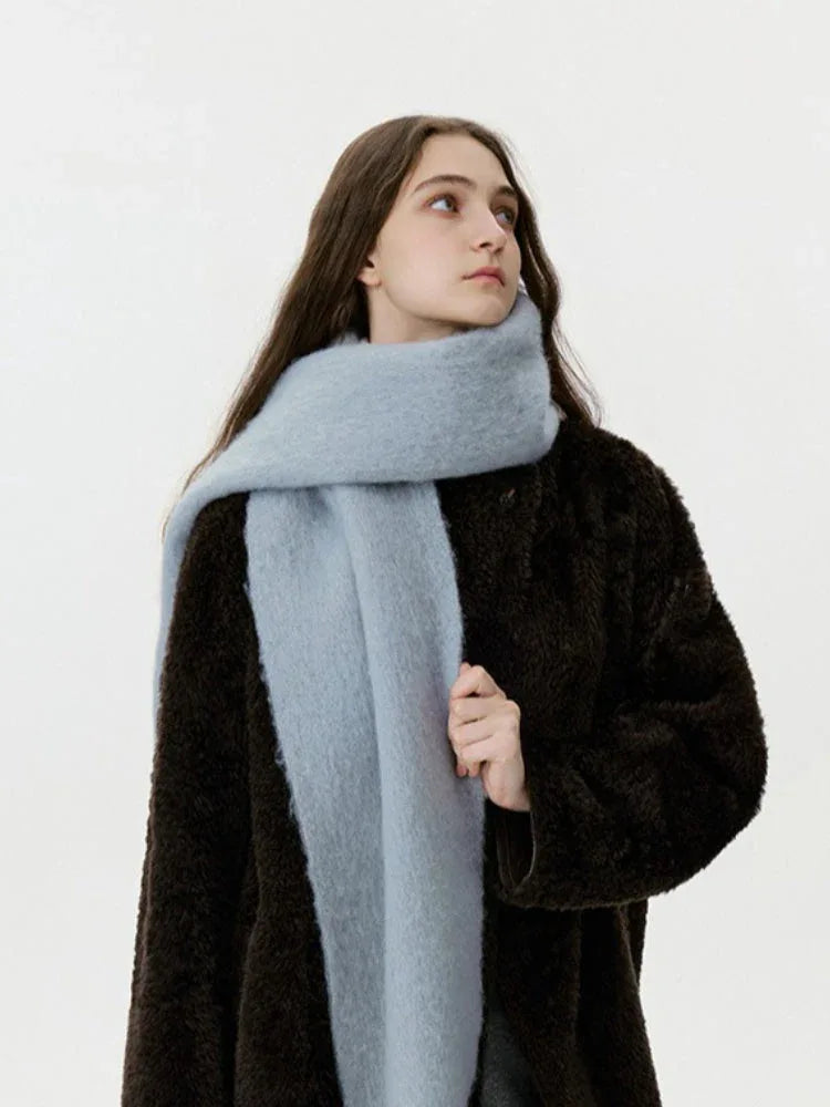 Close-up of a woman wearing a dark brown coat and a light blue scarf, looking upwards.