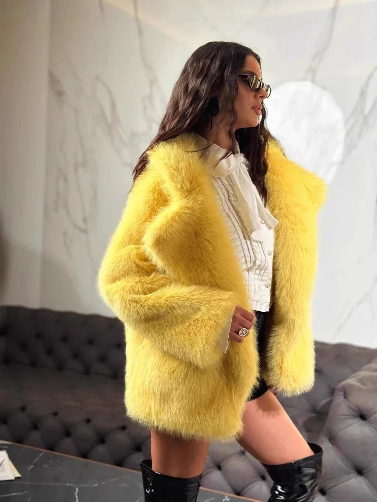 Woman wearing a yellow faux fur jacket, white ruffled shirt, black shorts, and black boots, with sunglasses and jewelry.