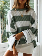 Woman wearing a green and white striped knit sweater with a crew neck and rolled-up sleeves, standing in front of a window, with one hand tucked into her sweater.
