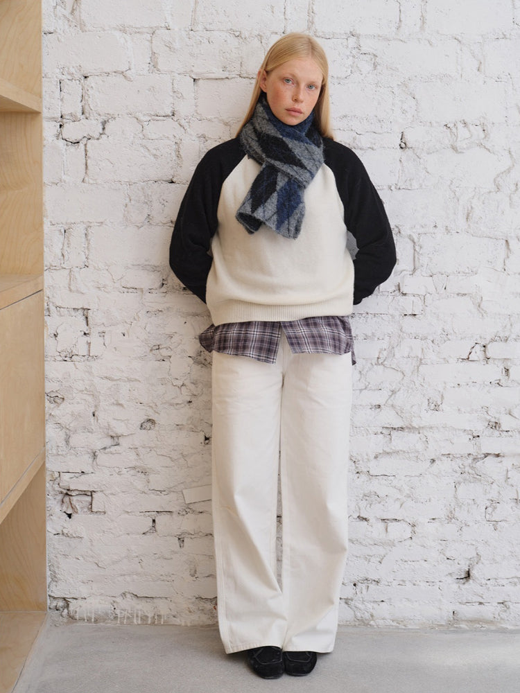 Model wearing a cream and black sweater with a striped scarf and white pants