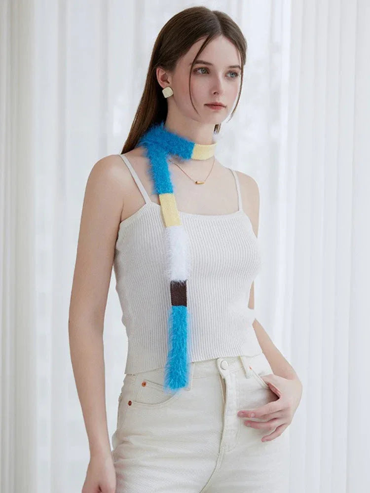 Model wearing a white ribbed tank top and off-white pants, with a long, fluffy, color-blocked scarf styled around her neck.