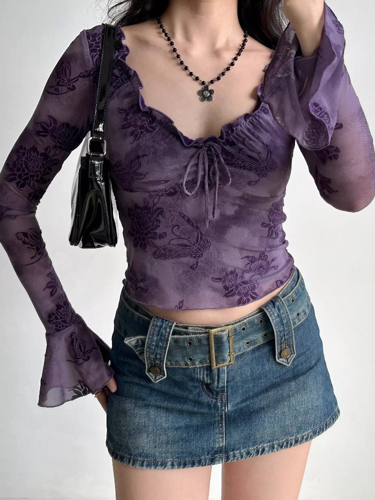 Full body shot of a woman wearing a purple sheer mesh top with a floral print, denim skirt, and a black handbag.