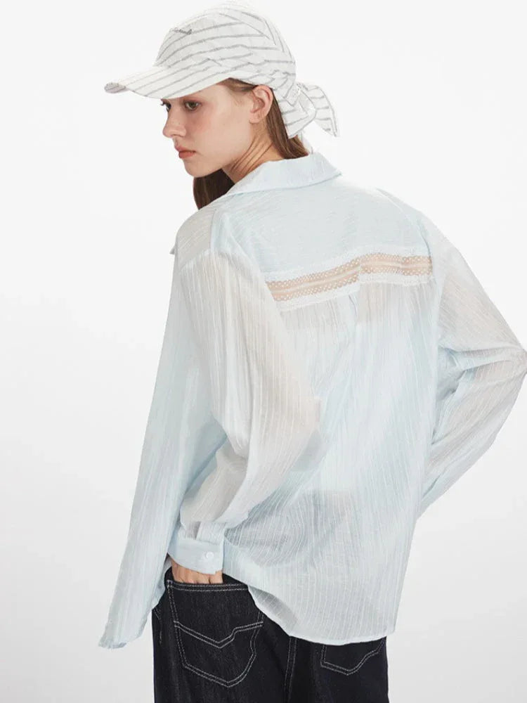 Close-up back view of a woman wearing a light blue sheer button-down shirt with lace detail on the back yoke, and dark wash wide-leg jeans.