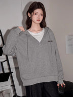 Woman wearing a grey V-neck oversized hoodie and black jeans, posing with a handbag.